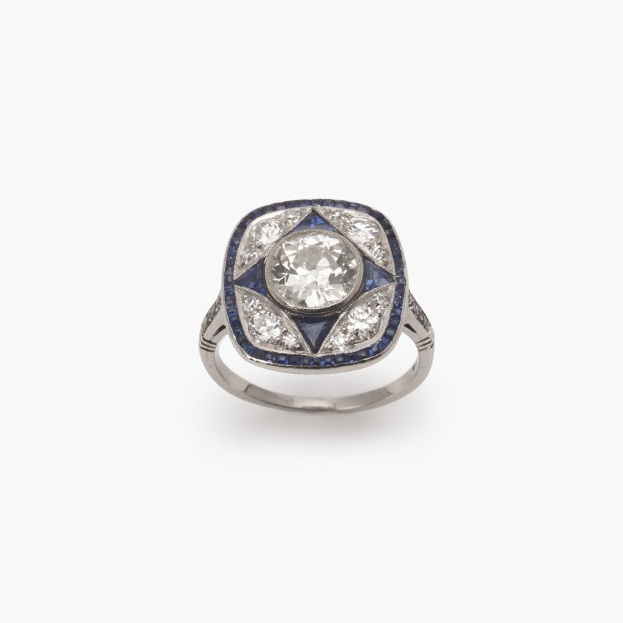 Een platina Art Deco ring, bezet met oud slijpsel briljant geslepen diamant en blauwe saffier in een geometrisch ontwerp. Vervaardigd omstreeks 1920.