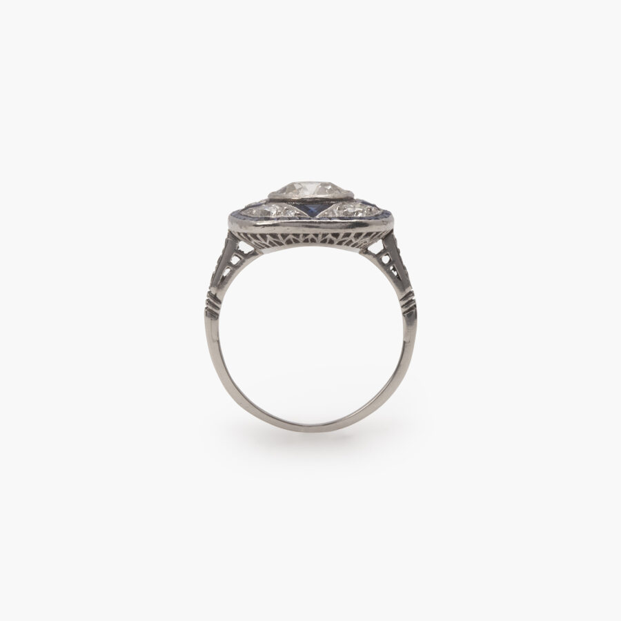 Een platina Art Deco ring, bezet met oud slijpsel briljant geslepen diamant en blauwe saffier in een geometrisch ontwerp. Vervaardigd omstreeks 1920.