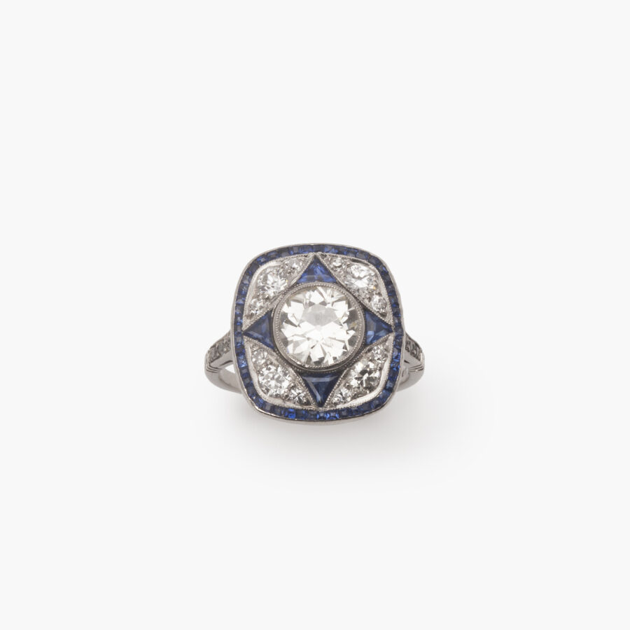 Een platina Art Deco ring, bezet met oud slijpsel briljant geslepen diamant en blauwe saffier in een geometrisch ontwerp. Vervaardigd omstreeks 1920.