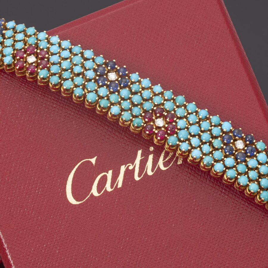 Een achttien karaat geelgouden armband bezet turkoois en met bloemvormen van robijn of blauw saffier en diamant. Gesigneerd Cartier, Italië omstreeks 1960.