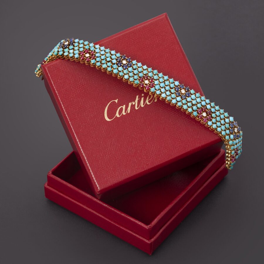 Een achttien karaat geelgouden armband bezet turkoois en met bloemvormen van robijn of blauw saffier en diamant. Gesigneerd Cartier, Italië omstreeks 1960.